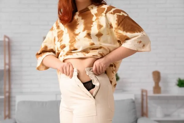 Image of woman trying to do her trousers up after pregnancy weight gain Carlton